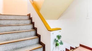 A staircase with a yellow handrail and a white wall with a plant decoration. - Kedkanok Apartment (Bangkok)