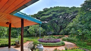 Un jardin avec un parterre de fleurs circulaire, une pergola et un grand arbre en arrière-plan.