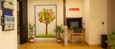 Un área de recepción con un cuadro grande de un árbol colorido, plantas en macetas, un escritorio con una computadora y un letrero que indica Netzone.