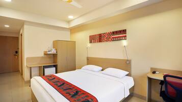 Habitación de hotel con cama, escritorio, armario, ventilador de techo y una obra de arte colgada en la pared.