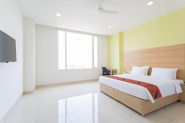 A modern hotel room with a large bed, a flat-screen TV, a ceiling fan, and a large window providing natural light. - Ginger Vapi (Vapi)