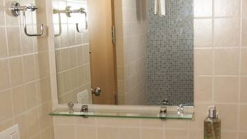A bathroom with a white sink, a glass shelf above it, a mirror, and a black trash bin labeled "DISPOSABLE BAG".