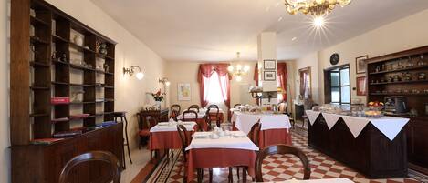 Un comedor con varias mesas dispuestas para el servicio, una amplia estantería de madera y un suelo a cuadros.
