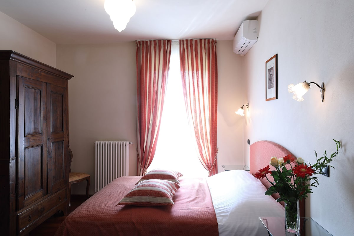 A bedroom with a bed, a wooden wardrobe, a radiator, and a window with curtains.