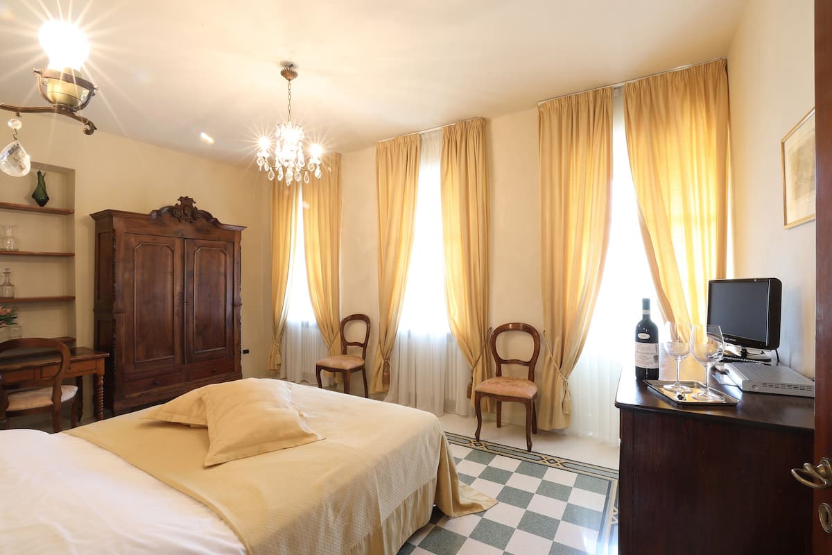 A hotel room with a bed, two chairs, a desk with a computer, a bottle of wine, and glasses.