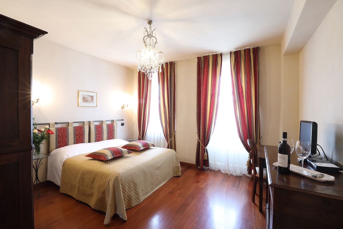 A hotel room with a bed, a desk with a computer, a wine bottle, and a glass.