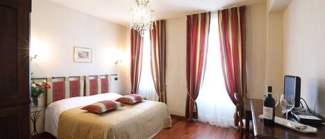 A hotel room with a bed, a desk with a computer, a wine bottle, and a glass.