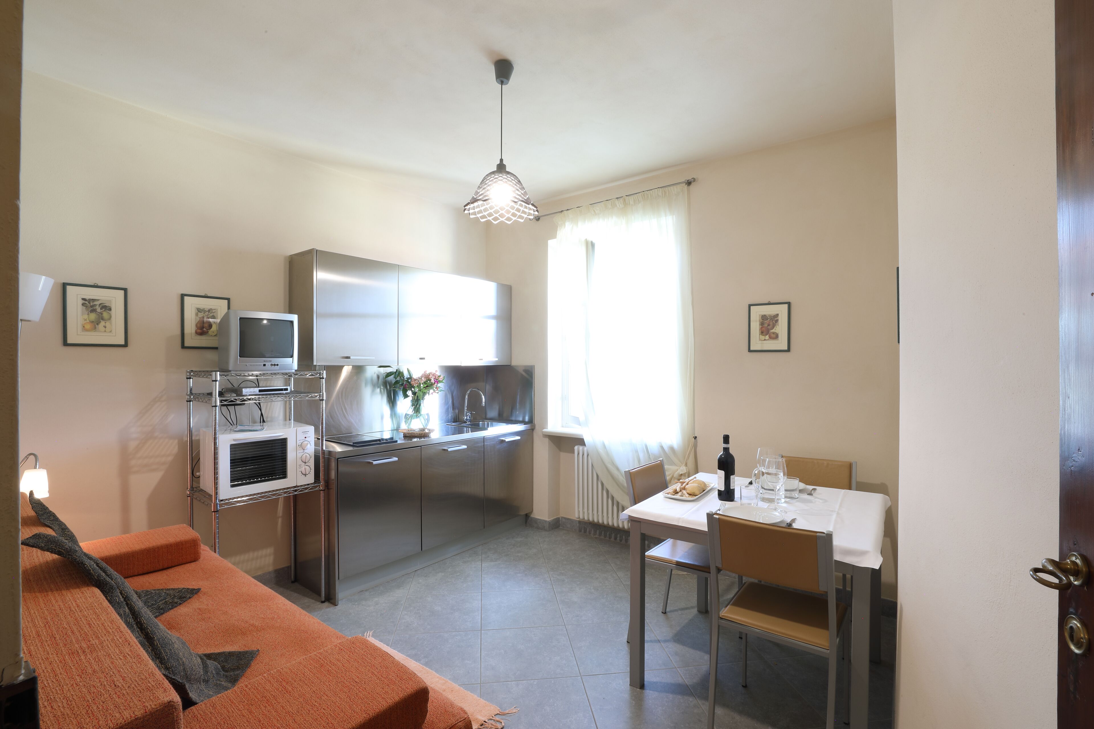 A compact kitchen with a microwave, oven, and sink. There is a dining table with chairs and a sofa in the foreground.