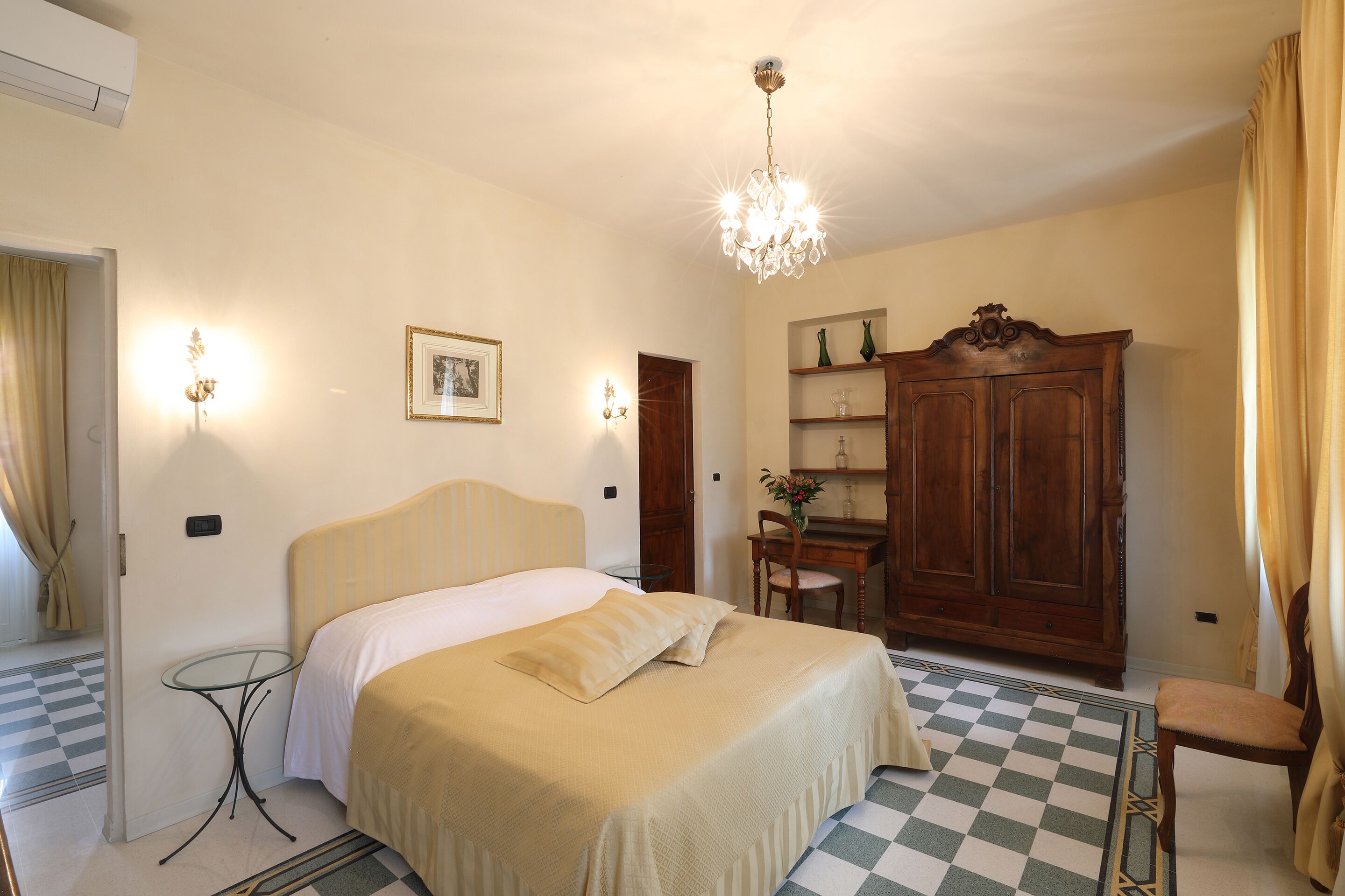 Ein Hotelzimmer mit Bett, Schreibtisch, Stuhl, Kleiderschrank und einer Chandelier.