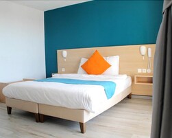 Una habitación de hotel moderna con una cama grande, un cabecero de madera y una pared azul decorativa.