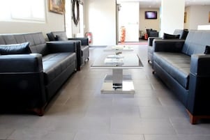 A modern lobby with two black leather sofas facing each other, a central coffee table, and a flat-screen TV on the wall.