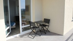 Un pequeño balcón con una mesa, dos sillas, una puerta corrediza de cristal y vistas al interior.