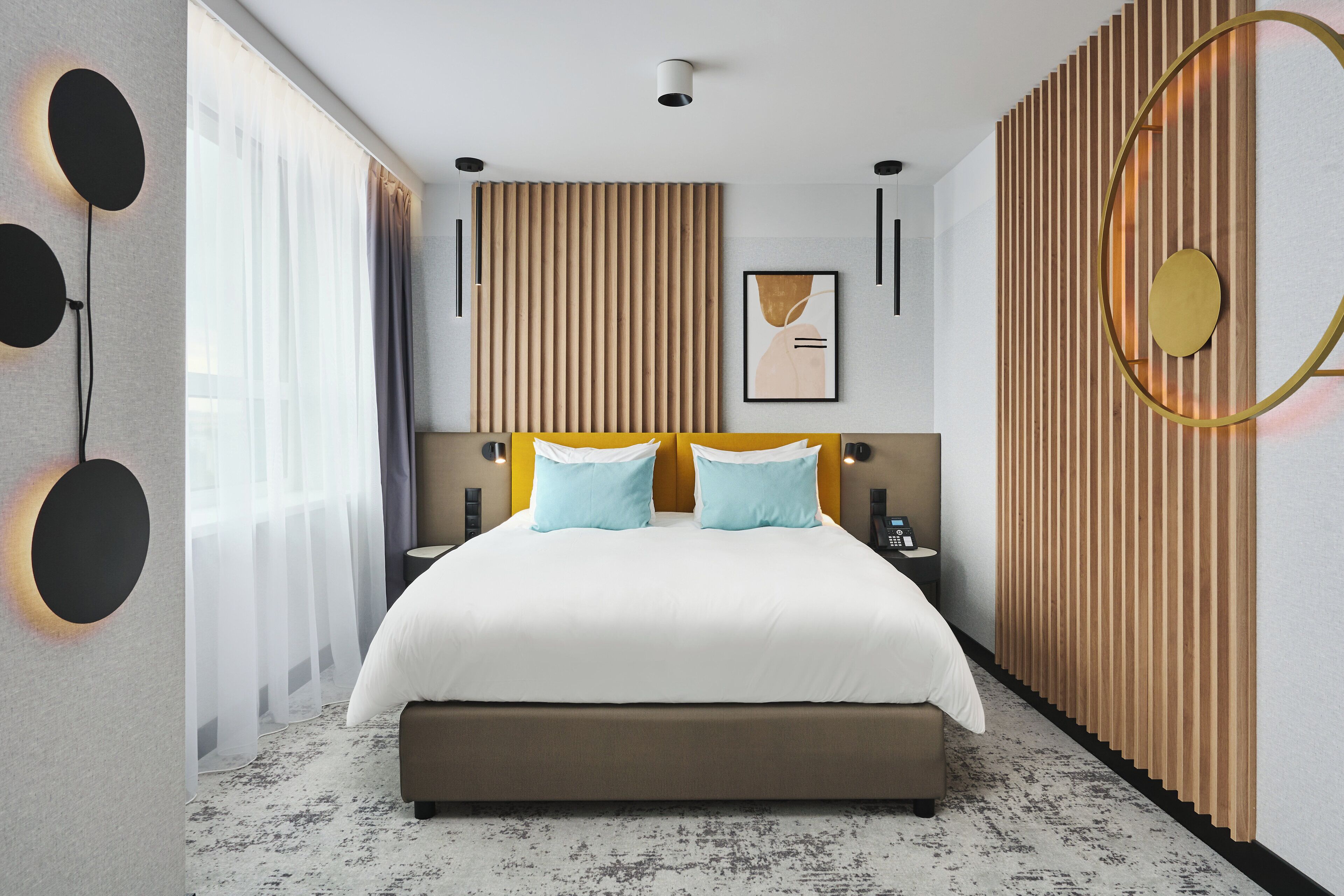 A modern hotel room with a large bed, a wooden panel wall, and a large window with curtains.