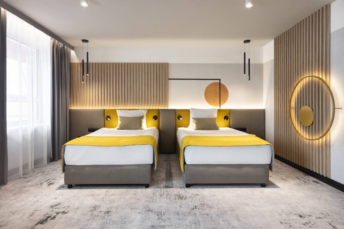 Una habitación de hotel moderna con dos camas, un ventanal con cortinas y una lámpara circular fijada a la pared.