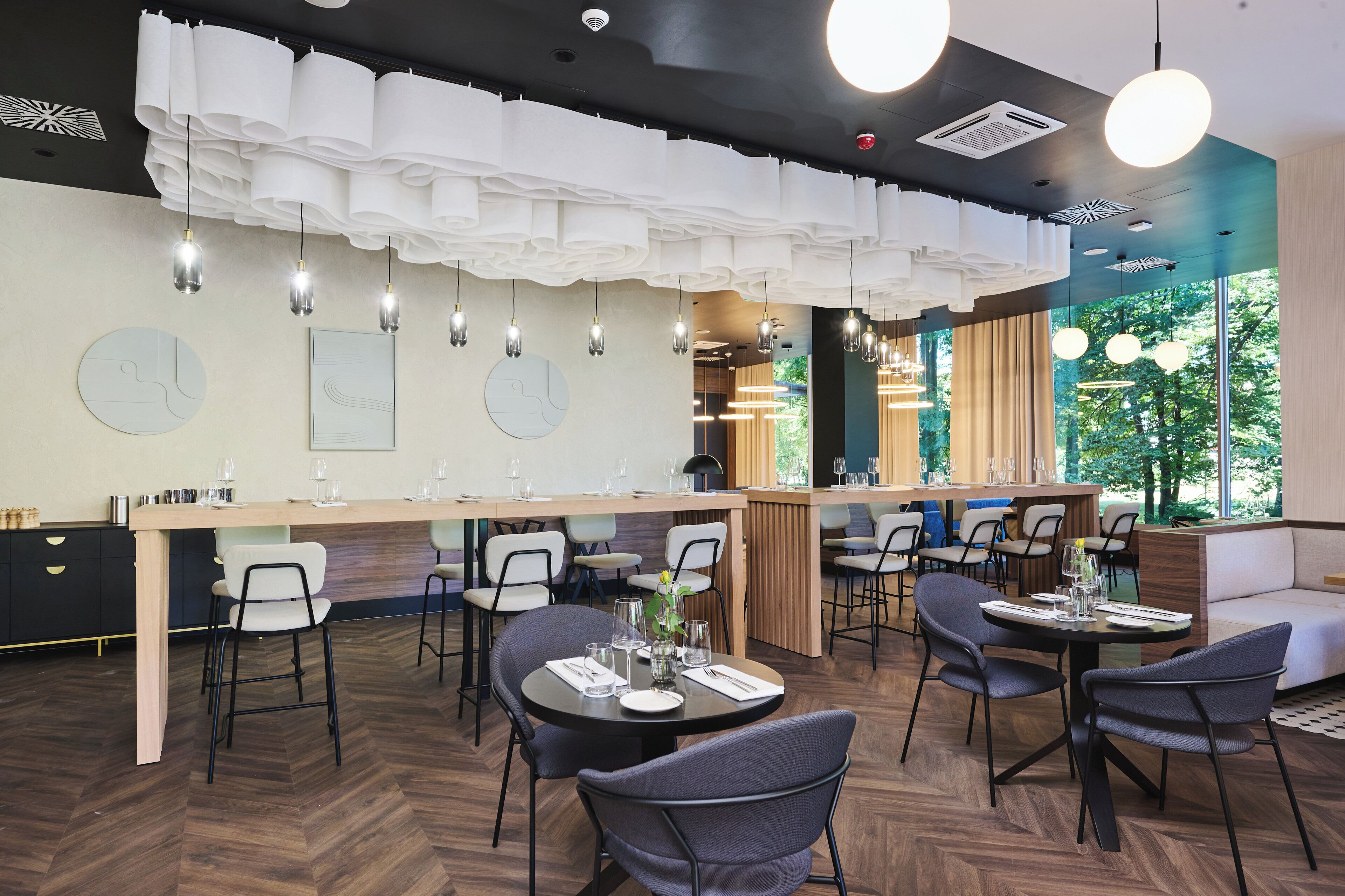 A modern restaurant with a long counter, multiple dining tables, and chairs.