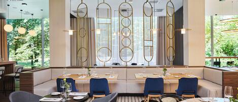 Un restaurante con una decoración moderna, que presenta una larga banqueta, mesas redondas e iluminación colgante.