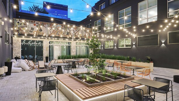 An outdoor patio area with tables and chairs, a wooden planter box, and string lights. - voco Katowice by IHG (Katowice)