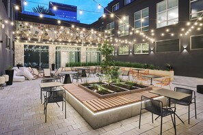 An outdoor patio with tables and chairs, string lights, and a planter with plants. - voco Katowice by IHG (Katowice)