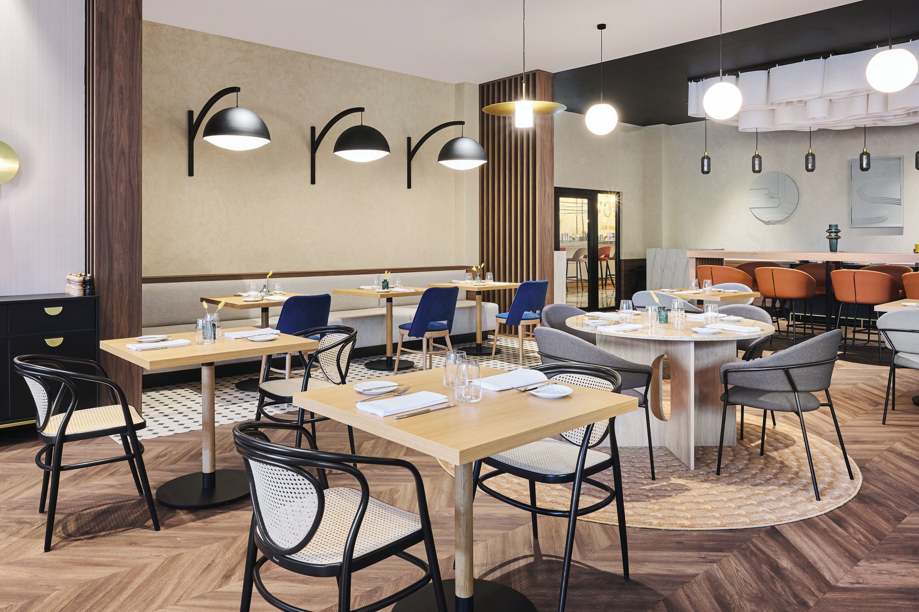 Un comedor moderno con varias mesas y sillas, iluminación colgante y suelo de madera.