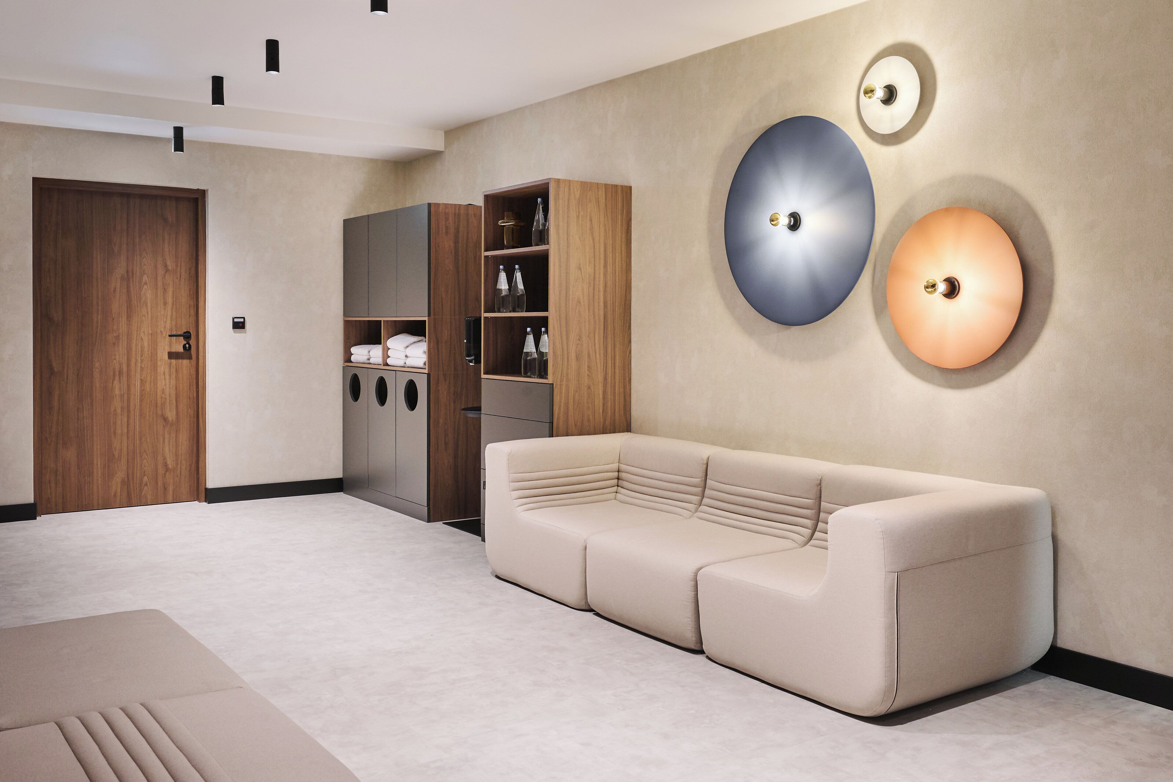 Una sala moderna con un sofá beige, un armario de madera e iluminación empotrada.