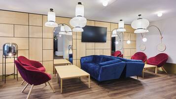 A modern interior with a blue sofa, red chairs, wooden tables, and hanging pendant lights.