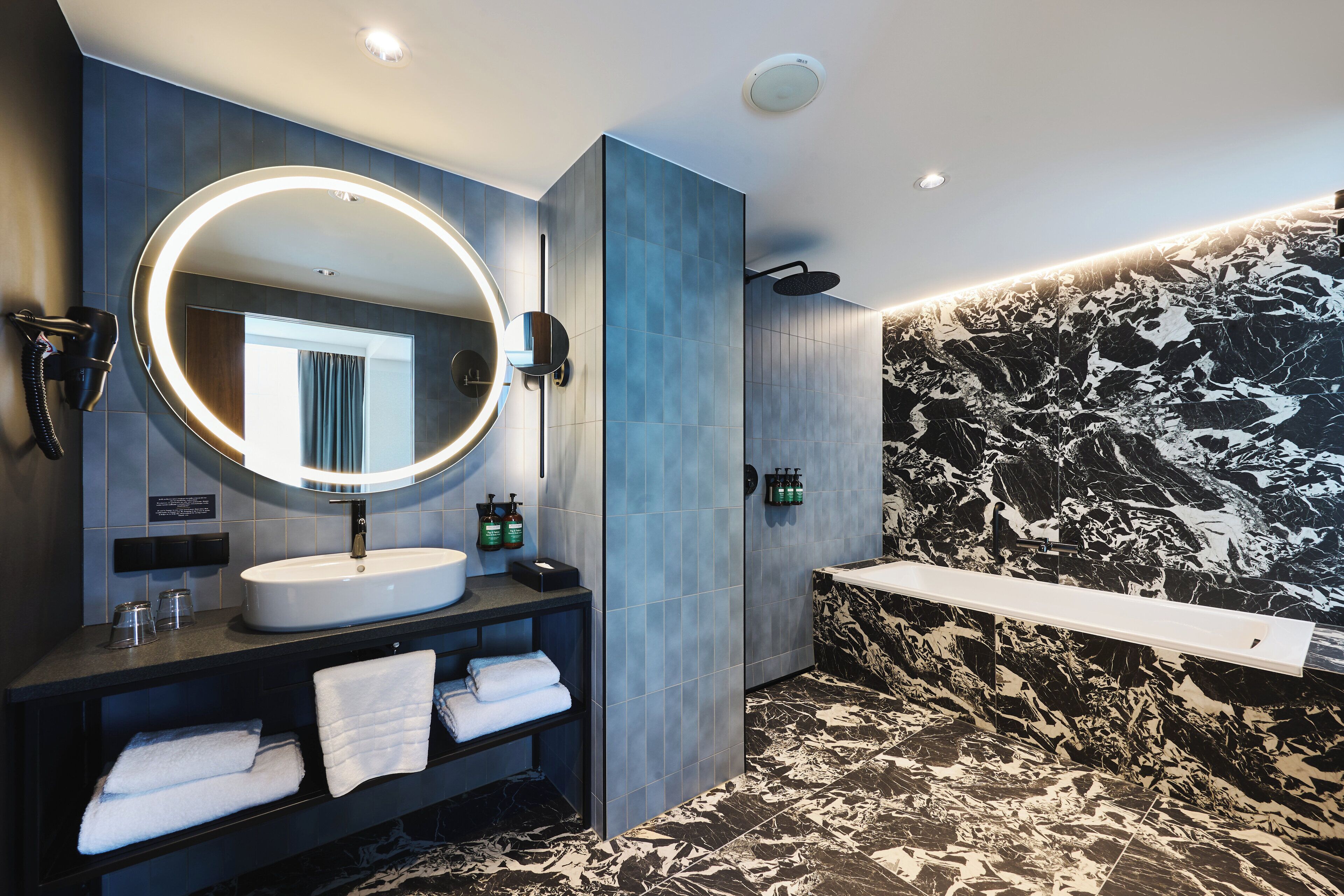A modern bathroom with a large mirror, a round vanity, a bathtub, and marble-patterned walls.