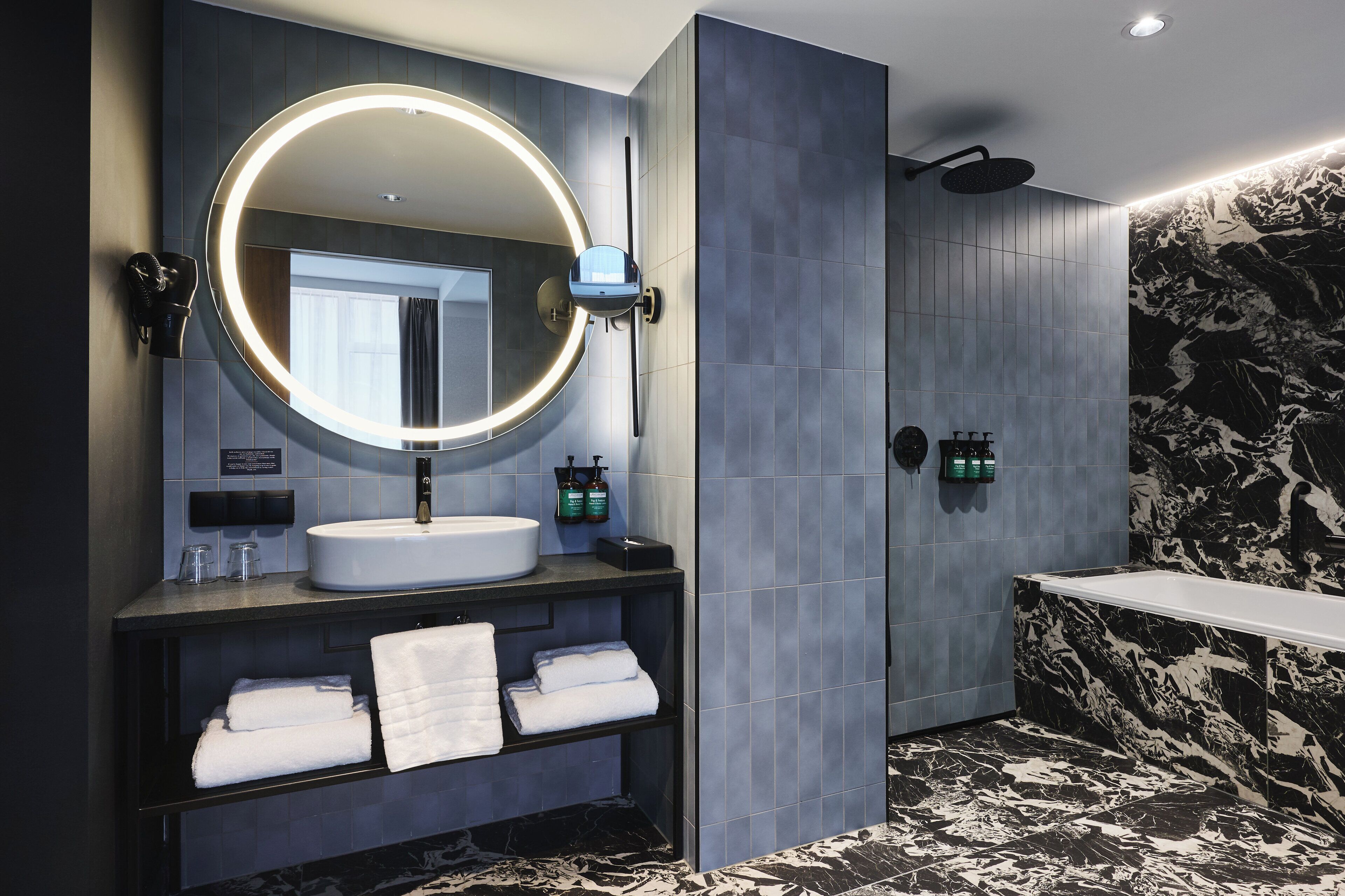 Un baño moderno con un espejo redondo, lavamanos blanco y pared de ducha de mármol blanco y negro.