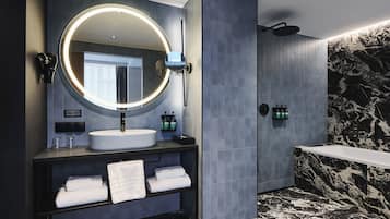 Un baño moderno con un espejo redondo, lavamanos blanco y pared de ducha de mármol blanco y negro.