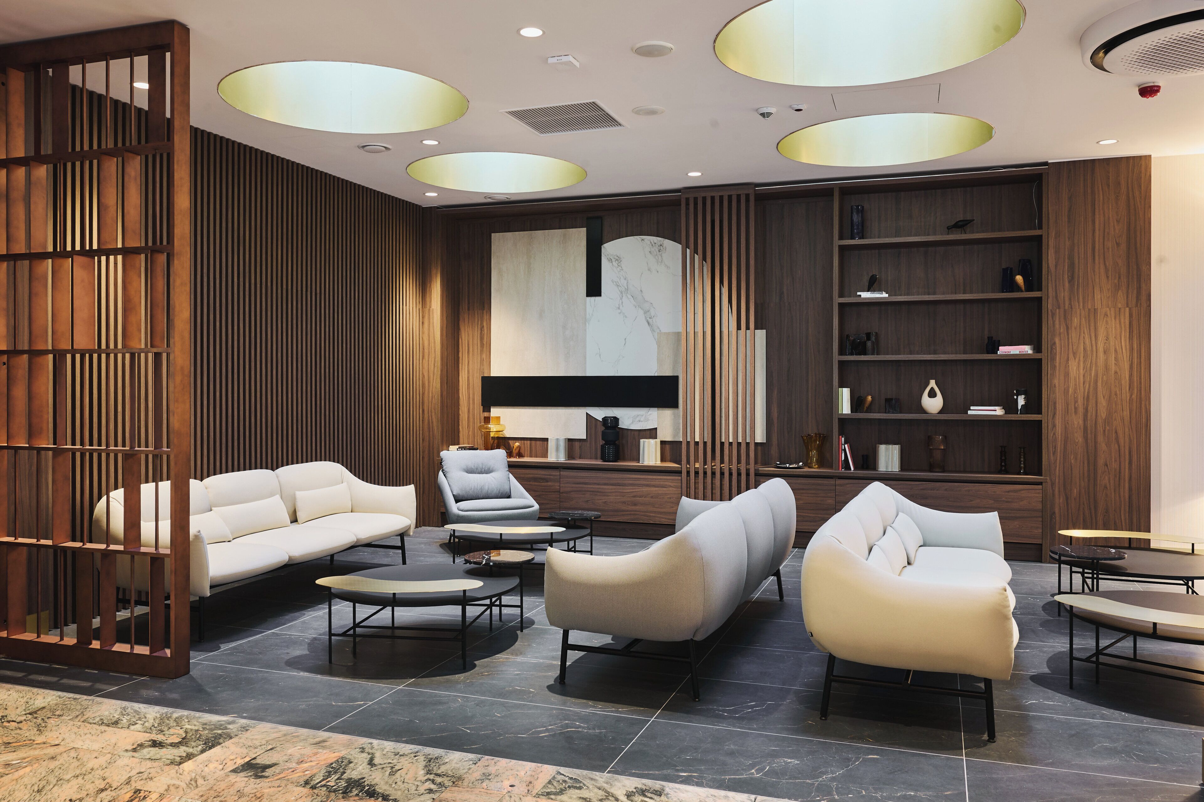 A modern lobby with a sectional sofa, armchairs, and a coffee table, featuring a wooden partition and a large abstract mural.