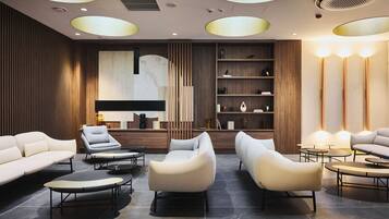 Een moderne lounge met banken, fauteuils en een salontafel, met een houten paneelwand en een accentmuur van marmer.