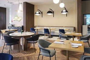 A modern dining area with round tables, blue chairs, and black pendant lights. - voco Katowice by IHG (Katowice)