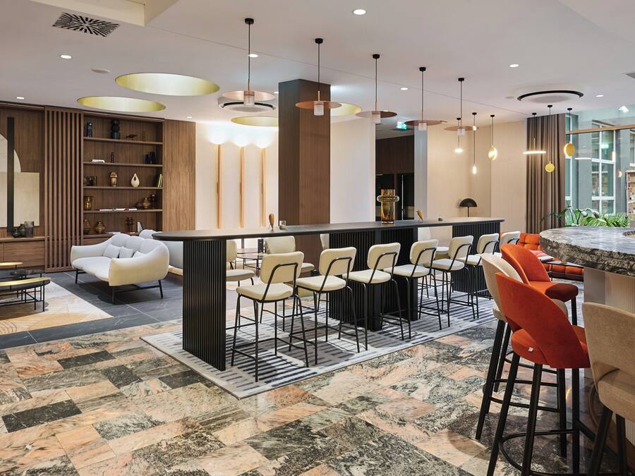 A modern bar area with a marble countertop, multiple bar stools, and pendant lighting.