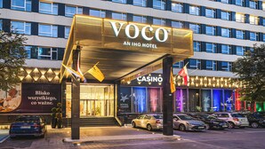 A hotel with a prominent "Voco An IHG Hotel" sign, a casino, and multiple cars parked in front. - voco Katowice by IHG (Katowice)