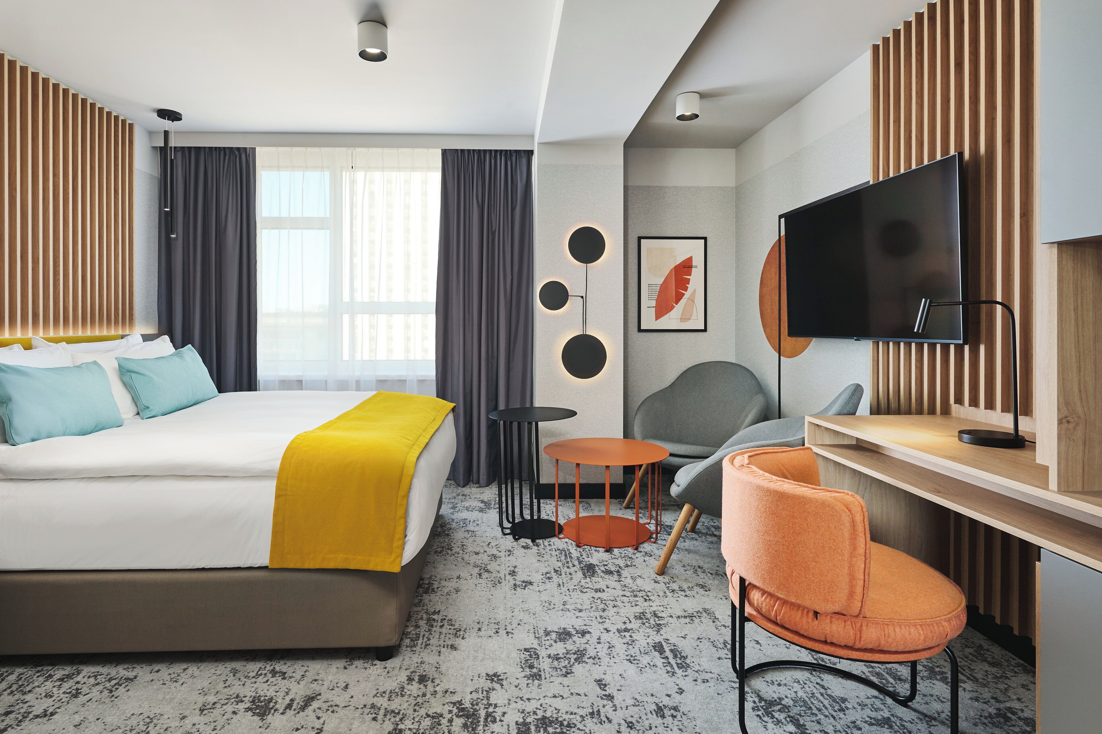 A modern hotel room with a large bed, a desk, a chair, a TV, and a window with curtains.