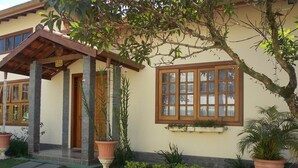 A house with a covered porch, a large window, and potted plants. - Pousada Sonhos (Ubatuba)