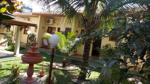 A courtyard with a fountain, palm trees, and a building with a tiled roof. - Pousada Sonhos (Ubatuba)