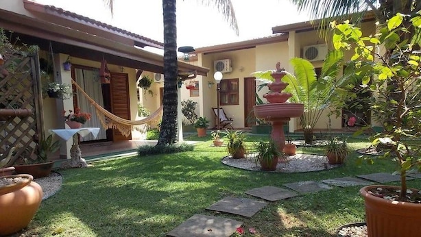 A courtyard with a hammock, potted plants, a fountain, and a palm tree. - Pousada Sonhos (Ubatuba)