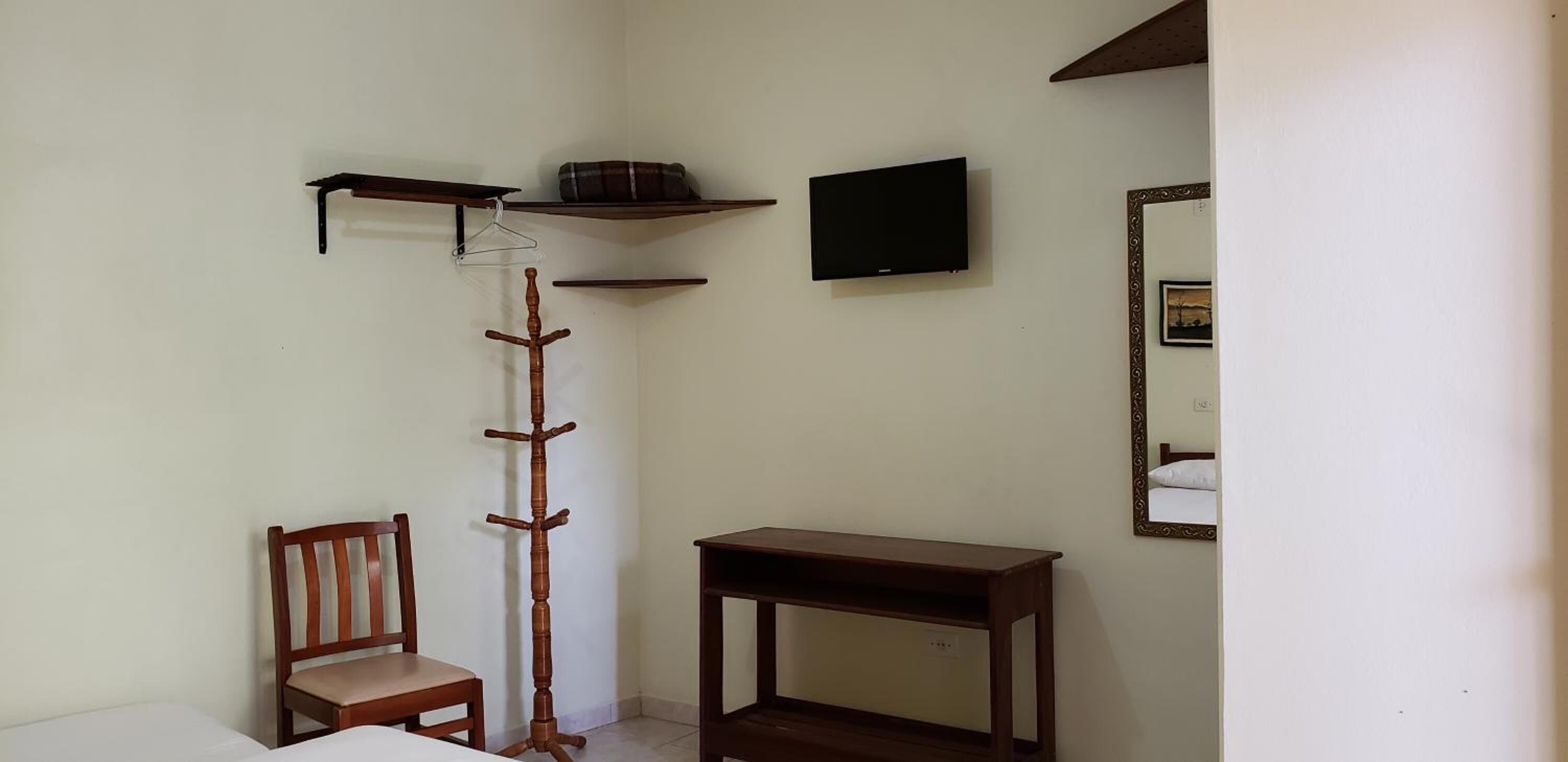 Una habitación con un perchero de madera, una silla, una mesita, un televisor y un espejo en la pared.