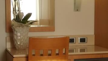 A wooden desk with a mirror above it, a vase with white flowers, and a wooden chair.