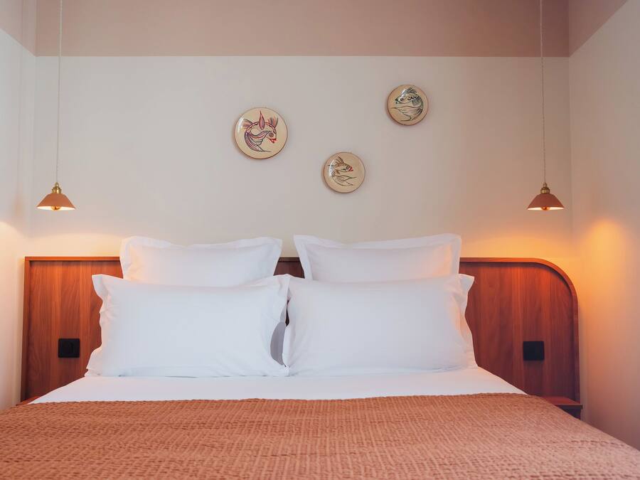 A neatly made bed with white linens and a brown throw, a wooden headboard, and three wall-mounted light fixtures with decorative plates.