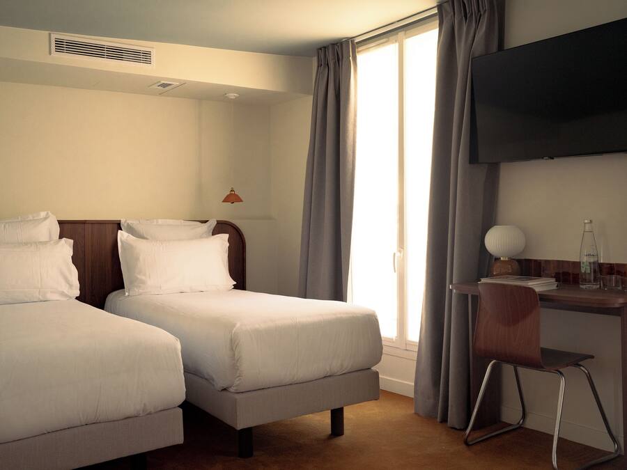 A hotel room with two beds, a desk with a chair, a television, and a window with curtains.