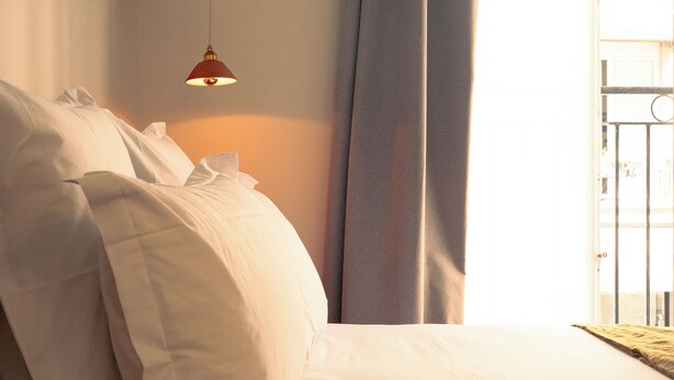 Un dormitorio con cama, lámpara colgante y vistas al exterior a través de una ventana con cortinas.