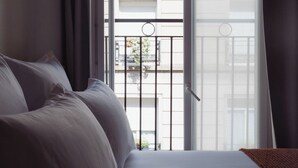 Una habitación de hotel con cama, ventana con cortinas y vistas a un balcón con barandillas.