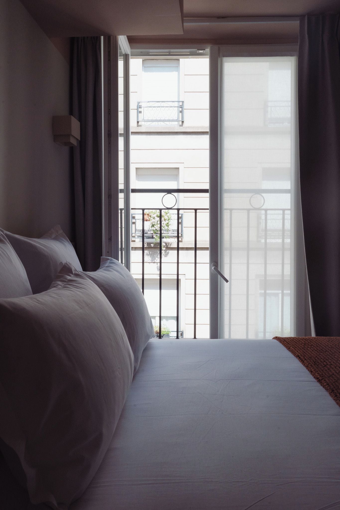 Una habitación de hotel con cama, ventana con cortinas y vistas a un balcón con barandillas.