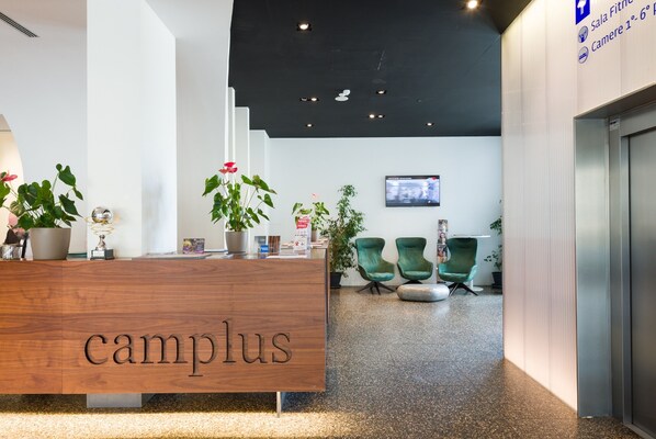 A reception desk with the word "campus" on it, surrounded by potted plants and green chairs.