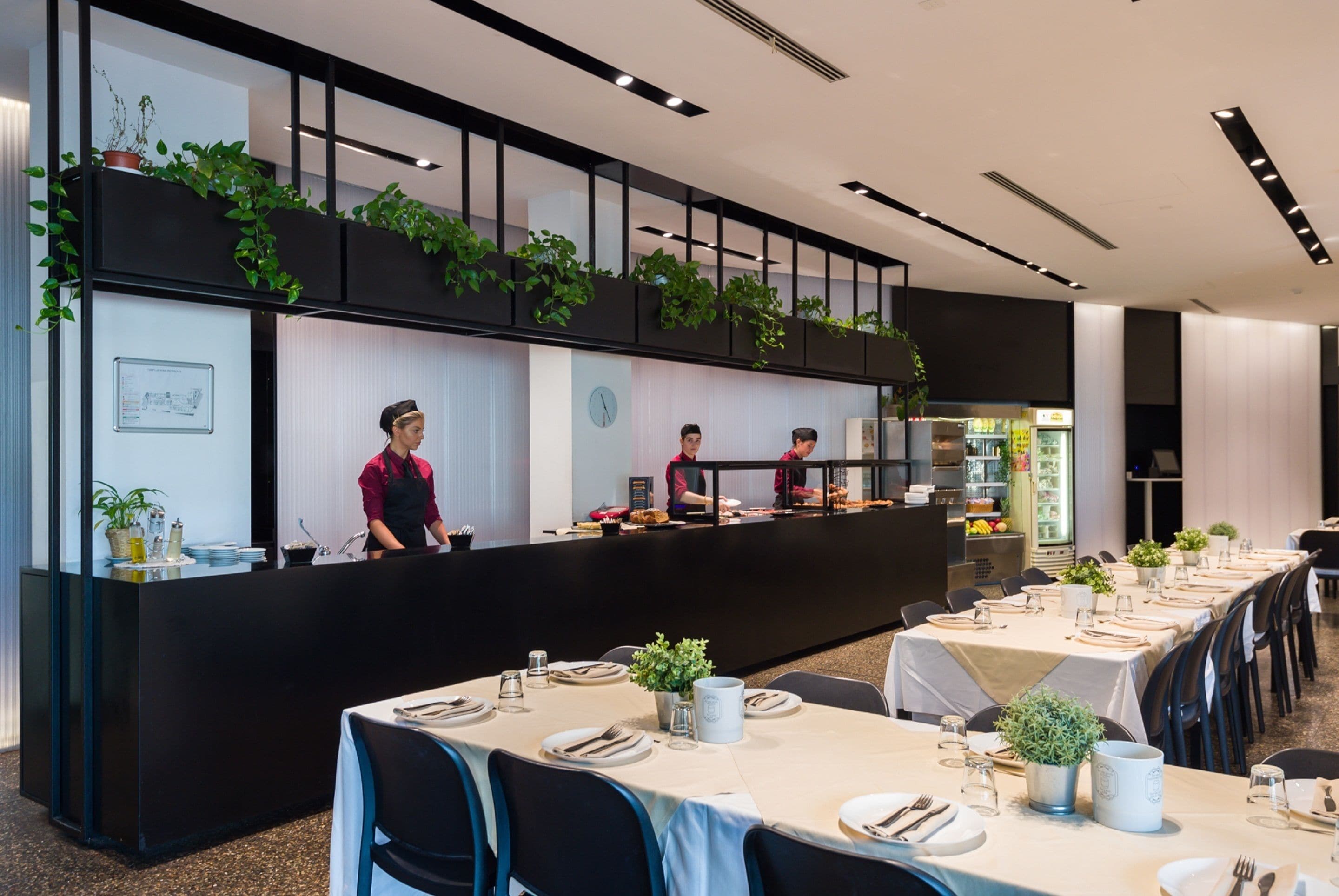 A modern restaurant with a black counter, staff serving, and tables set for dining.