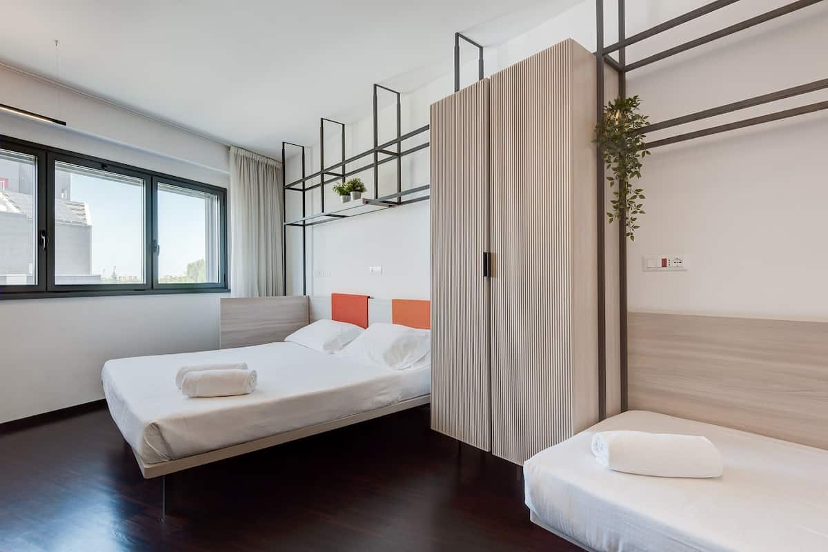 Una habitación de hotel moderna con dos camas, un ventanal grande, una planta y un separador de madera.