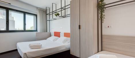 A modern hotel room with two beds, a large window, a plant, and a wooden partition.