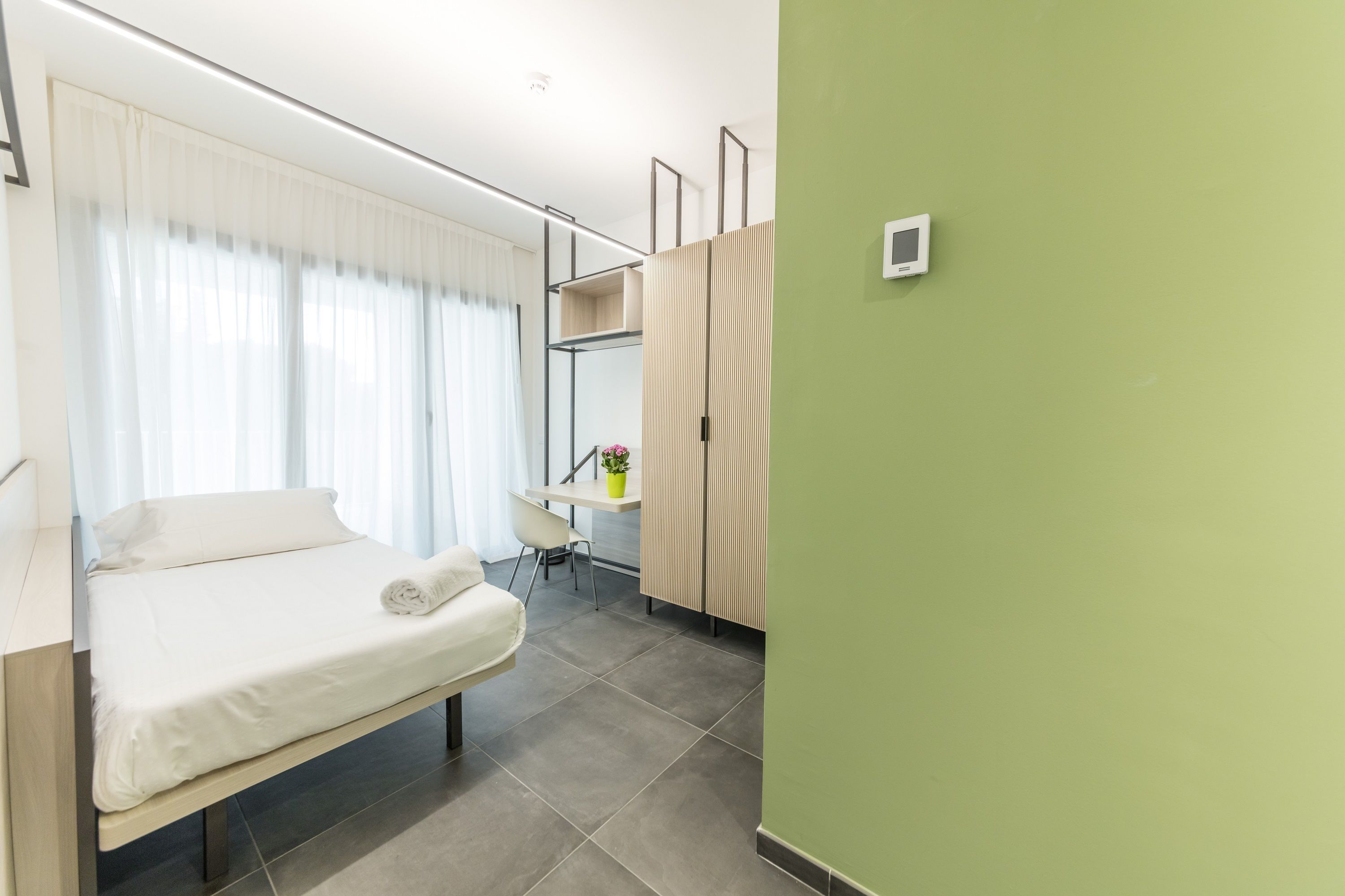 Una habitación de hotel moderna con una cama, un escritorio y una pared verde.