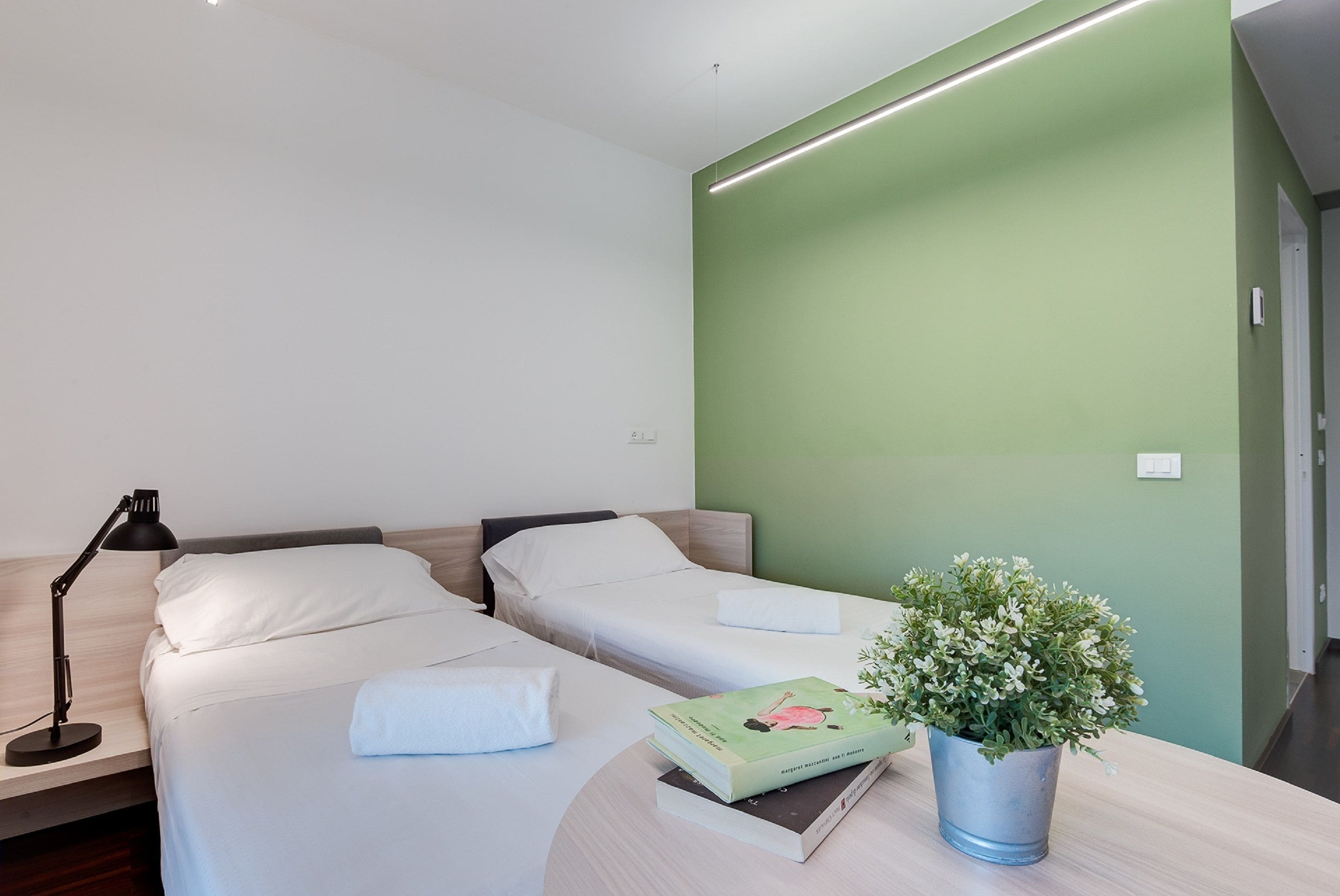 A hotel room with two beds, a desk with a lamp, and a potted plant.